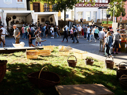 Willow baskets displayed on the grass at the Lichtenfels basketry festival, with visitors walking through the market in the background. / リヒテンフェルスのかご編みフェスティバルで、芝生の上に並べられたやなぎのかごと、奥を行き交う来場者たち。