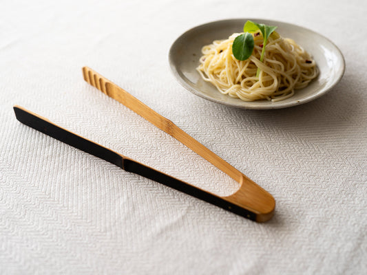 Smoked bamboo tongs on a tablecloth / 炭竹のトングをテーブルクロスの上に置いた様子