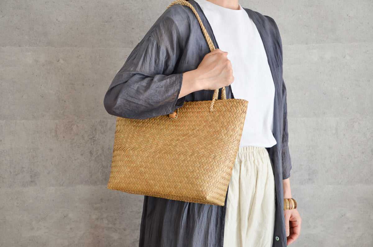 Krajood grass slim tote bag with button held on shoulder / カチューの留め具付きスリムトートを肩に掛けた様子