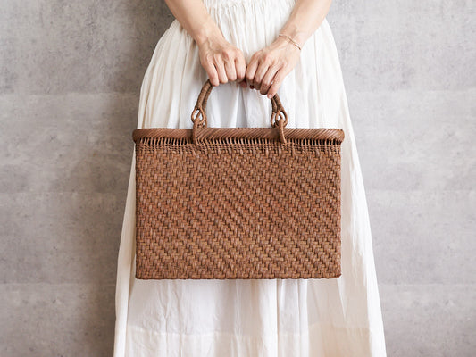 A person holding an A4 grapevine tote basket with swing handles by its handles / やまぶどうのリング手A4トートバッグを手に持っている様子