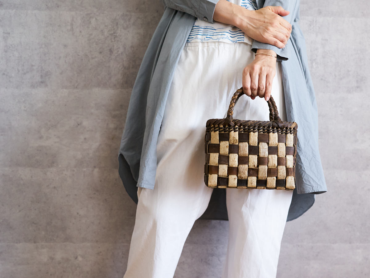 A person holding a tiny walnut bark checker basket by its handle / くるみのtiny手提げを手に持っている様子