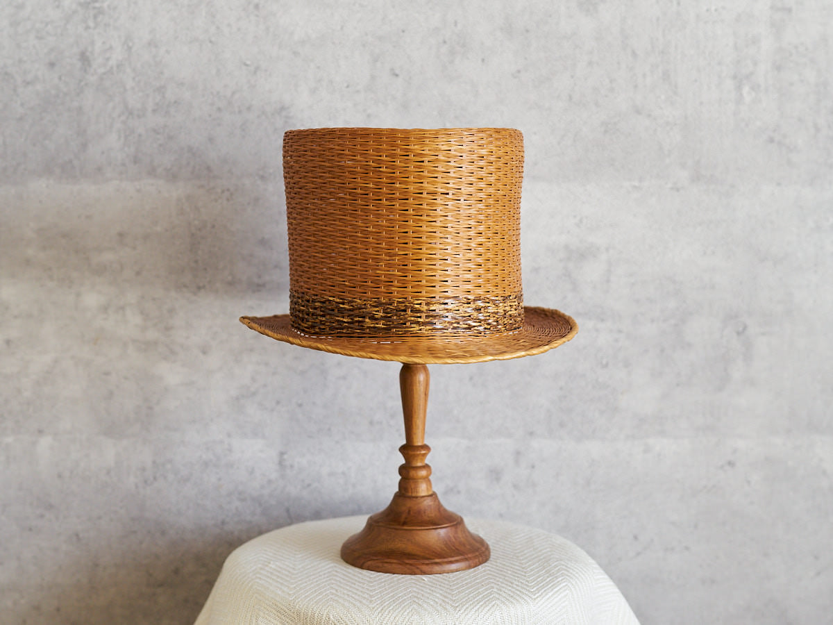 Urushi-lacquered carbonized bamboo hat on a wooden stand / 漆仕上げの炭化竹の帽子を木製のスタンドにのせた様子