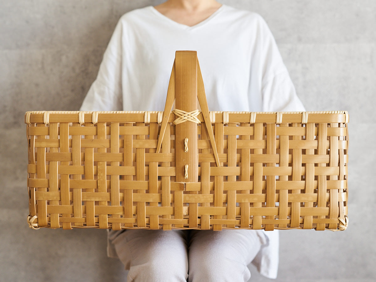 Large handled basket made of carbonized bamboo, resting on a person's lap / 炭化竹の手つき大籠を膝にのせている様子