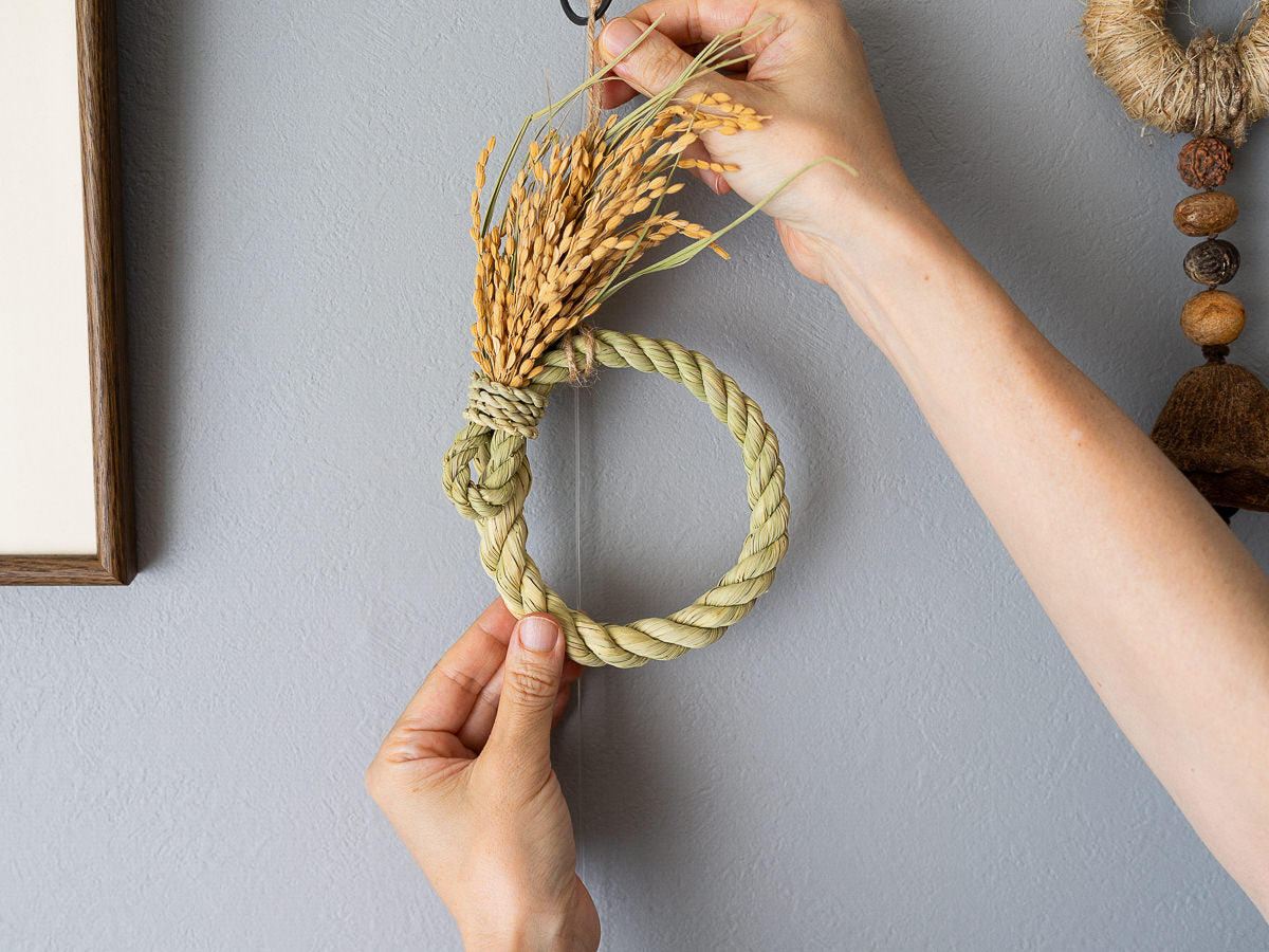 Rice straw shimekazari being hung on a wall by hand / 稲わらのしめかざり（円満）を手で壁に掛けている様子