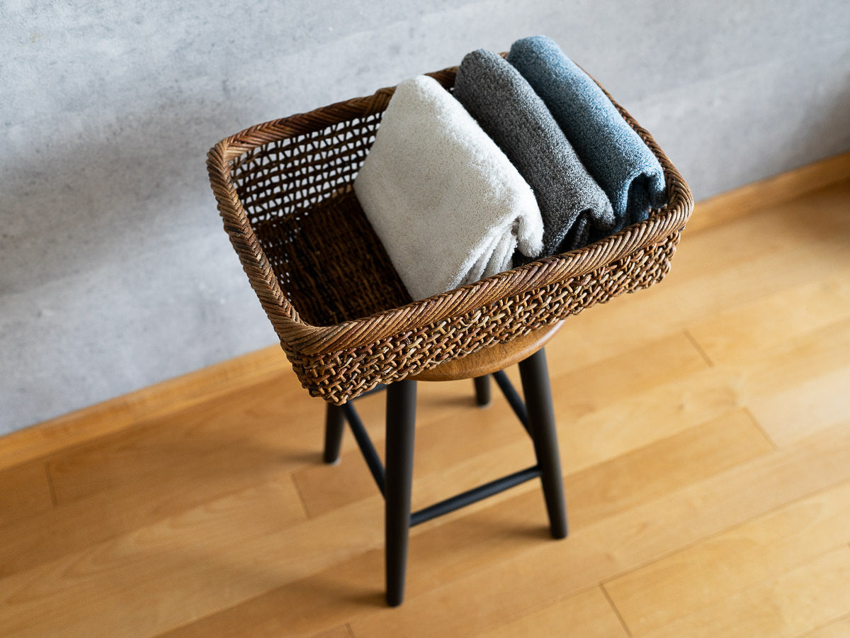 Akebi rectangle basket with sukashi weave on a stool / タオルが入ったあけびのすかし編み角かごがスツールの上に置かれている様子