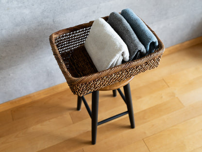Akebi rectangle basket with sukashi weave on a stool / タオルが入ったあけびのすかし編み角かごがスツールの上に置かれている様子