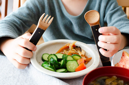 Smoked bamboo children’s spoon and fork held in hand / 炭竹の子どもスプーンとフォークを持っている様子