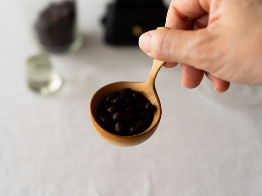 Smoked bamboo coffee measuring spoon held in hand / 炭竹のコーヒーメジャーに豆を入れて持っている様子