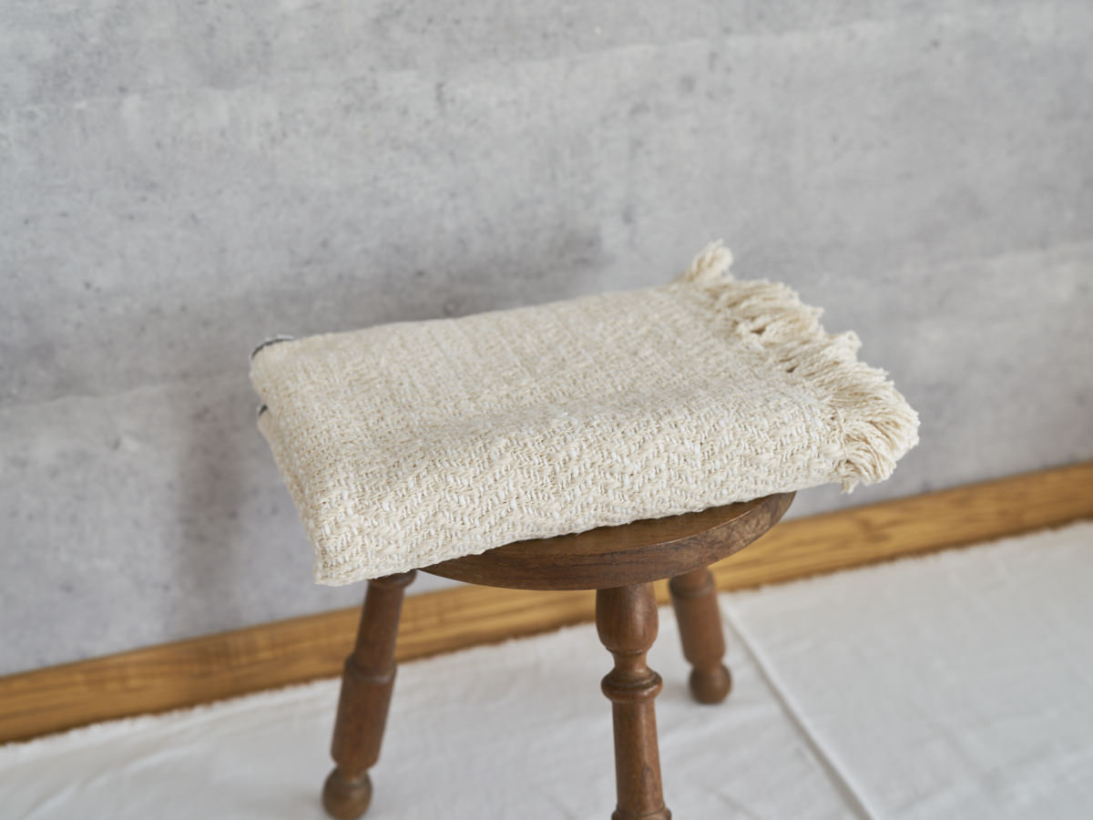Woven cotton stole placed on a wooden stool / コットンのガラ紡ストールをスツールに置いた様子