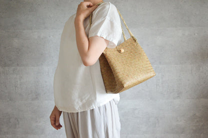 Krajood grass cube handbag with closure carried on shoulder / カチューのキューブ型の留め具付きかごバッグを肩に掛けた様子