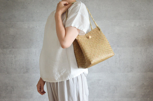 Krajood grass cube handbag with closure carried on shoulder / カチューのキューブ型の留め具付きかごバッグを肩に掛けた様子